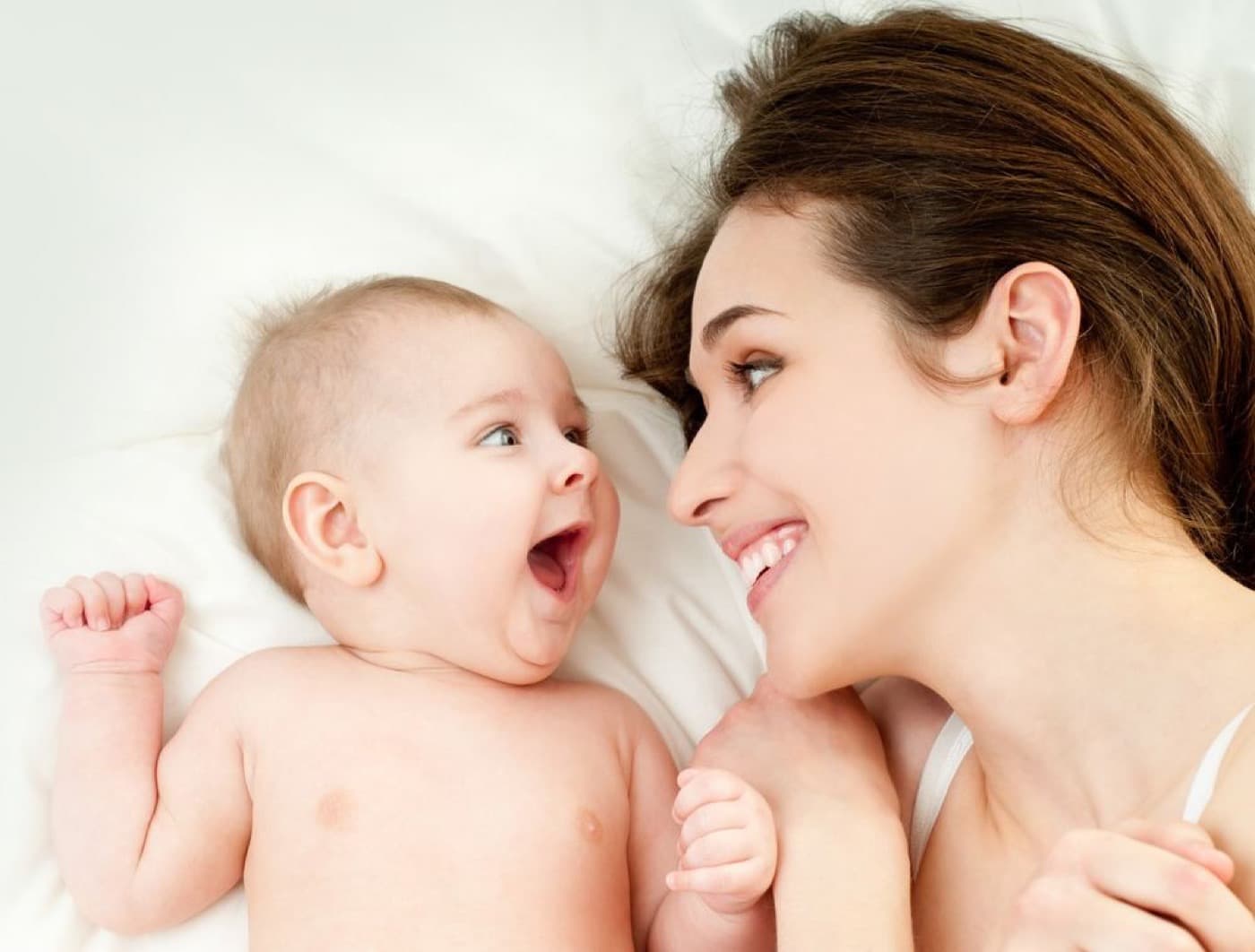 Moeder en baby liggen samen op bed en kijken elkaar lachend aan